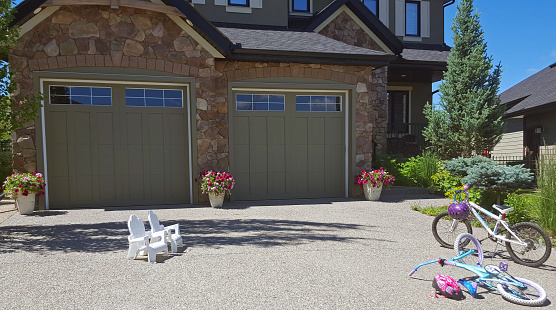 Calgary,Alberta,Canada- July 7,2018: Partial bottom view of modern home with two garage doors and driveway. Two kid's bikes and two kid's Adirondack chairs laying in driveway.