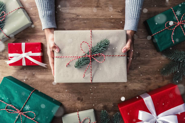 istock Woman hands giving Christmas gift box on wood table 995116578