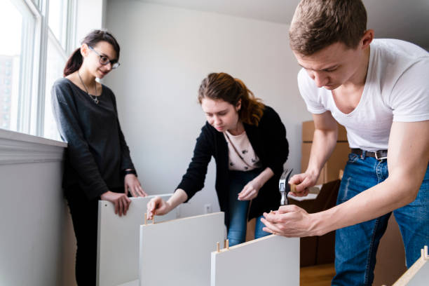 the family moving in to the new apartment. the young 30 years old man and two teenage girls, sisters, unboxing and assembling furniture. - independence lifestyles smiling years imagens e fotografias de stock