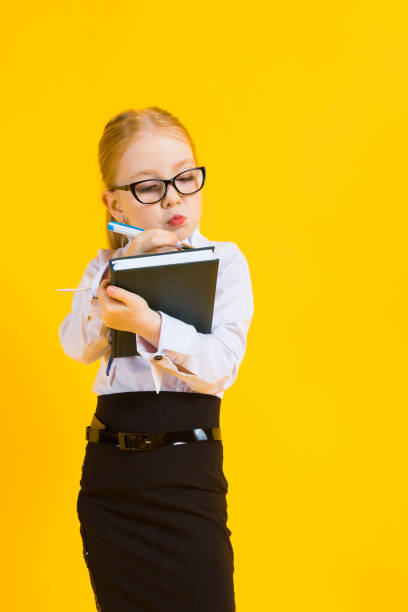 Girl with red hair on a yellow background. A charming girl in transparent glasses writes a pen in her notebook. Portrait of a beautiful girl in a white blouse and black skirt. see through leggings stock pictures, royalty-free photos & images