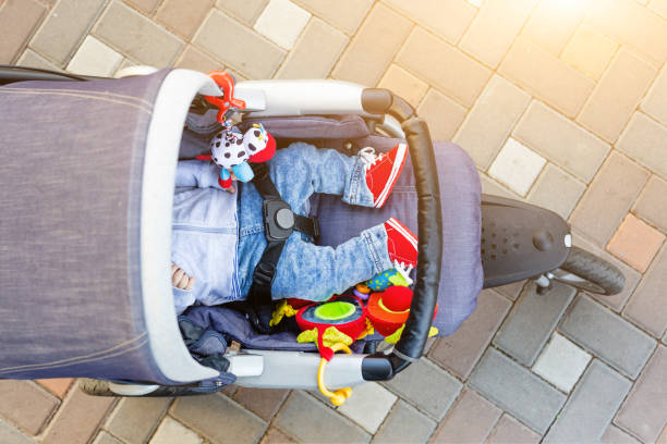 baby schlafen dreirädrigen kinderwagen im freien. kind im hellen lässigen kostüm liegt am großen komfortablen kinderwagen. eltern gehen mit kutsche im stadtpark. ansicht von oben - sportkinderwagen stock-fotos und bilder