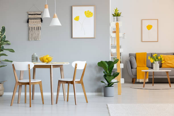 two white lamps above a round dining table in open space apartment interior with yellow blanket on gray sofa. real photo - wall flower sunny temperate flower imagens e fotografias de stock