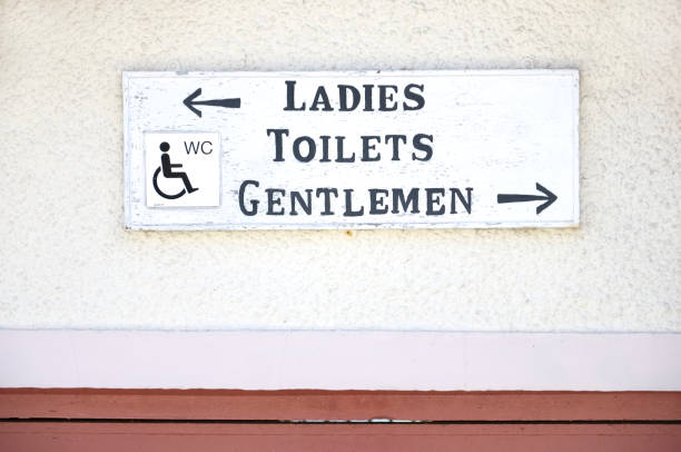 This public restroom sign was nailed to the side of a wooden structure.  The sign points the way to available facilities.  The paint is fading and weather worn.