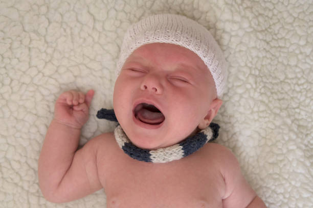 istock A newborn baby in hat and scarf is crying on a light background 995231362