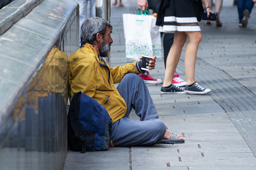 Vienna, Austria - July 7, 2018: male foreign beggar sitting in shopping street of Mariahilfer Strasse. Around are walking people for shopping