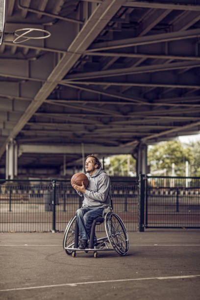 Wheelchair using young man during an outdoor urban basketball training session  on a streetball court