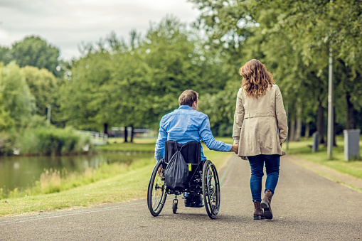 Wheelchair using young man and his girlfriend walking together through a city park on a sunny afternoon