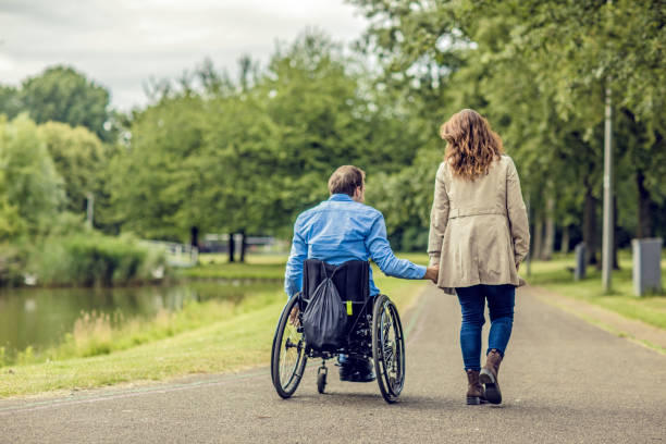Wheelchair using young man and his girlfriend holding hands whilst walking together through a city park stock photo