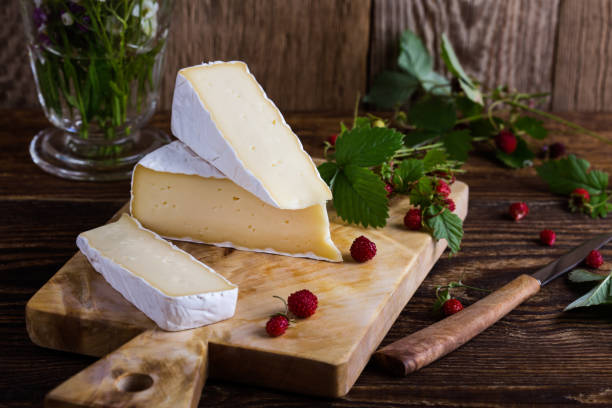 French brie cheese, wild strawberries and white purple wild flower bouquet French brie cheese, wild strawberries and white purple wild flower bouquet on rural wooden table brie stock pictures, royalty-free photos & images
