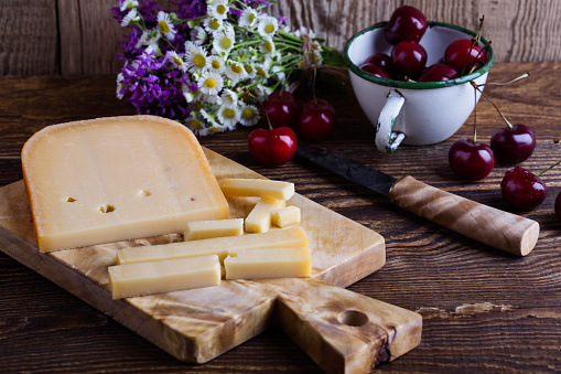 Traditional Dutch semi hard cheese served with sweet cheeries on rural table with summer wild flower