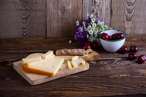 Traditional Dutch semi hard cheese served with sweet cheeries on rural table with summer wild flower
