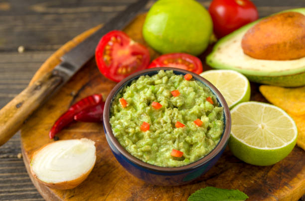 istock Guacamole in blue bowl on natural rustic desk with ingredient: lemon, tomatoes, peppers around. 995310088