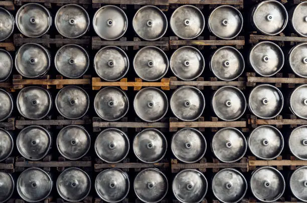 Stack of shiny stainless steel beer kegs outside in factory