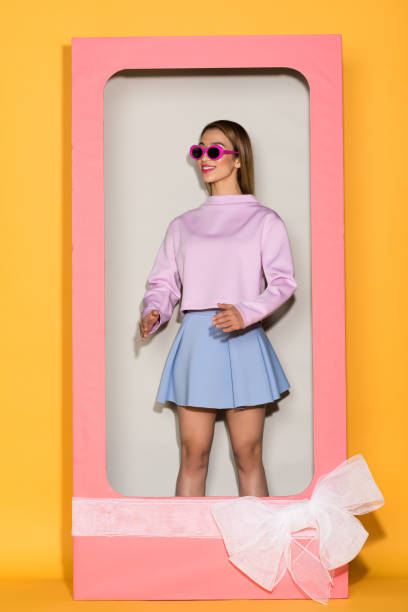 stylish female model in sunglasses standing in decorative box with box on yellow background stylish female model in sunglasses standing in decorative box with box on yellow background doll stock pictures, royalty-free photos & images