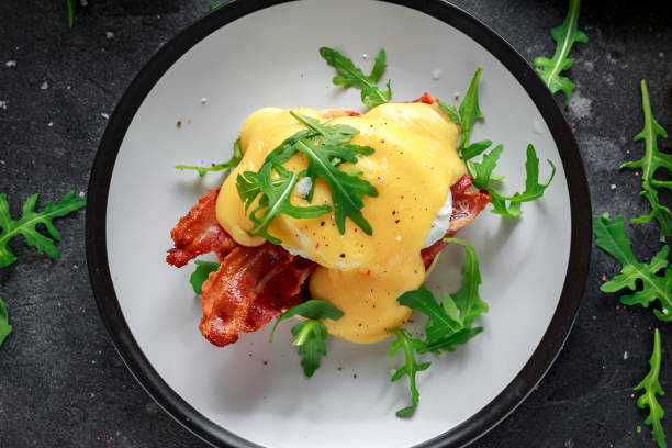 istock Eggs Benedict on english muffin with crispy bacon, wild rocket salad and hollandaise sauce 995319920