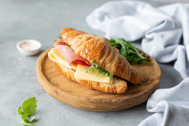Croissant sandwich with cheese, ham and arugula Croissant sandwich with cheese, ham and arugula on wooden cutting board, gray concrete background. Selective focus. Tasty breakfast sandwich or snack croissant stock pictures, royalty-free photos & images