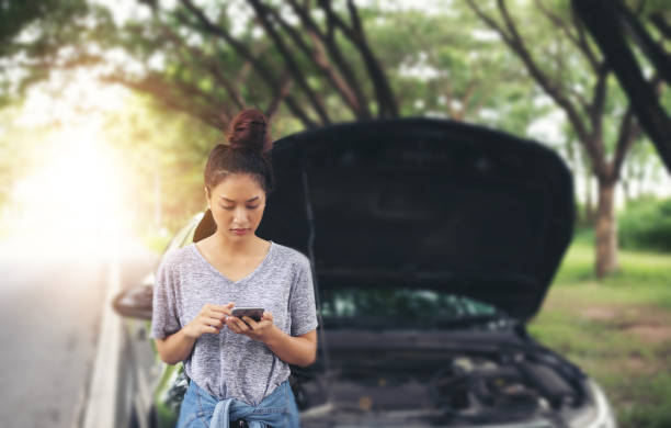 asian woman using mobile phone while looking and stressed man sitting after a car breakdown on street - avaria no carro imagens e fotografias de stock