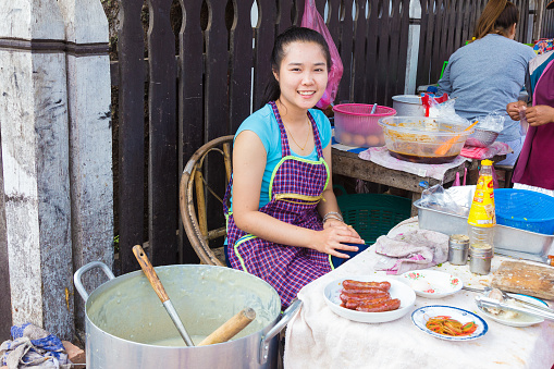 LUANG PRABANG, LAOS - 30 June 2018 - Happy congee or porridge female seller sits and waits for her customer at her food stall in Luang Prabang, Laos on June 30 2018