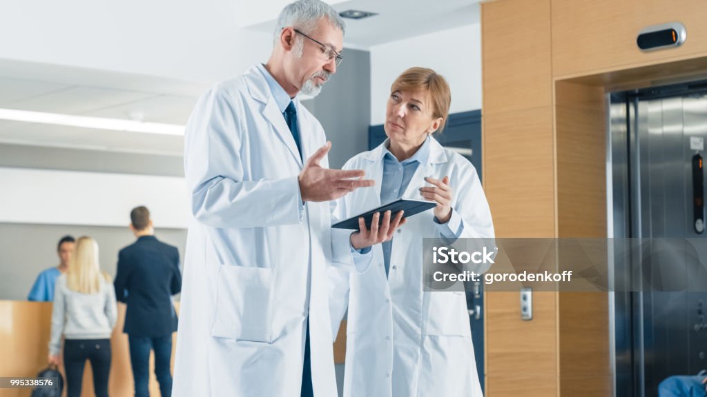 Haben Sie in der Krankenhaus-Ärzte Diskussion beim Tablet-Computer verwenden. Im Hintergrund Patienten und medizinisches Personal. Neue moderne voll funktionsfähige medizinische Einrichtung. - Lizenzfrei Gehen Stock-Foto