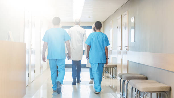 vista posteriore del team di medici, infermieri e assistenti che camminano attraverso il corridoio dell'ospedale. personale medico professionista che lavora, salva vite umane. - doctor healthcare and medicine human resources teamwork foto e immagini stock