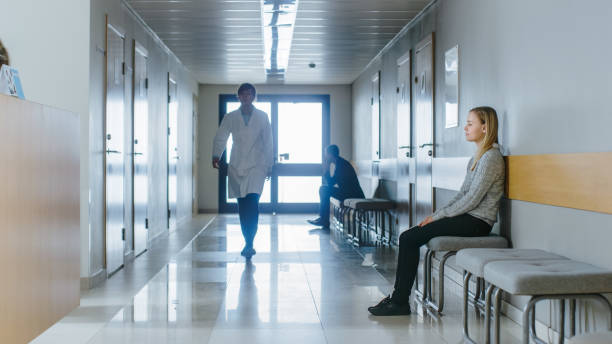 busy hospital hallway. medical personnel, doctors, nurses, surgeons walking, female patient waiting her turn. modern medical facility. - esperar imagens e fotografias de stock