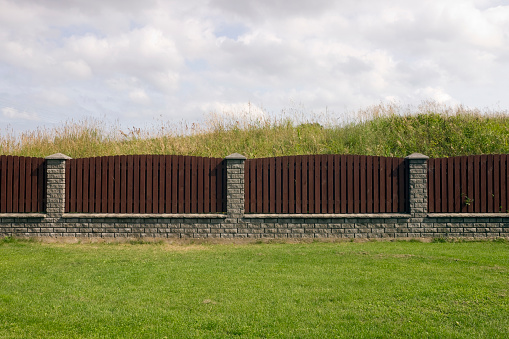 Long  brown wooden  fence from vertical  pine planks and  gray  bricks.