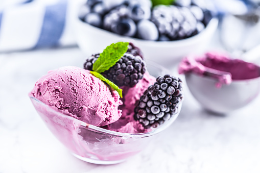 Blueberry and blackberry ice cream in bowl with frozen fruits.