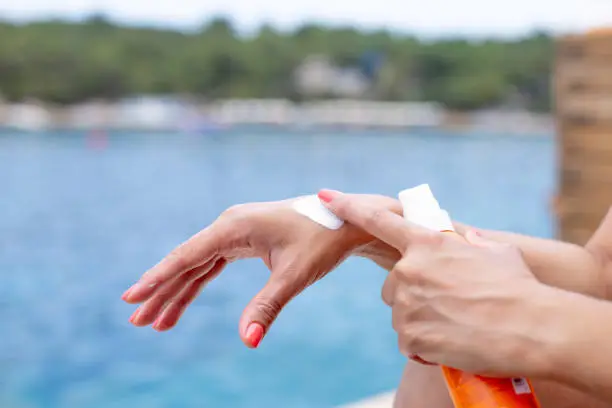 A girl on the beach applies sunscreen on her hand to protect the skin from sunburn. The concept of the season of holidays.