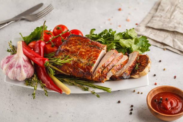istock Roasted pork with thyme, rosemary, garlic and tomato sauce on a white dish, white background, copy space. 995402512