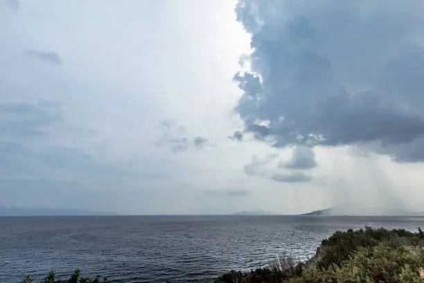 The beginning of the storm on the sea. The streams of rain fall into the open sea. The rain and thunderclouds on the sea bay.