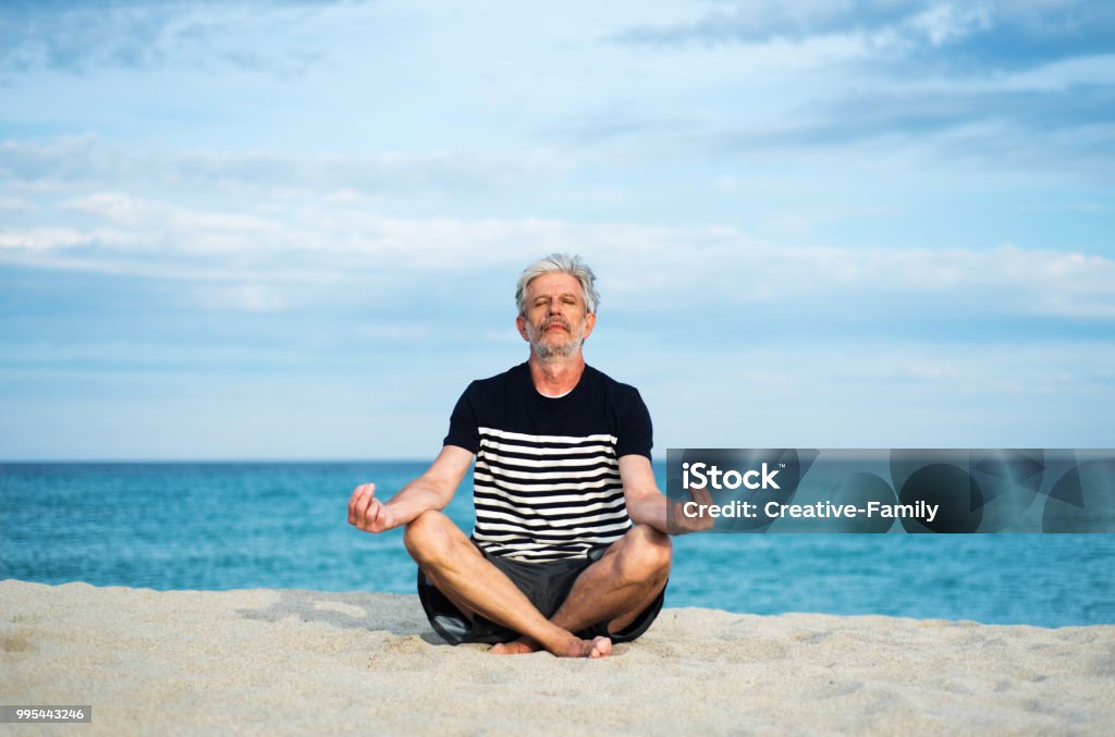 Senior man meditating on the beach Senior man meditating on the beach, summer vacation workout 60-69 Years Stock Photo