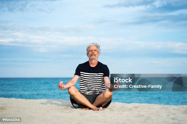 Senior Man Meditating On The Beach Stock Photo - Download Image Now - 60-69 Years, Active Lifestyle, Active Seniors