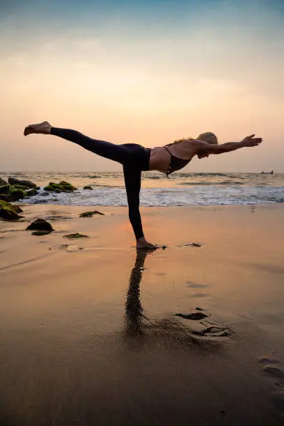 Photo of Middle age woman in black doing yoga on sand beach in India