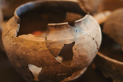 an old clay jug with large cracks stands on the shelf