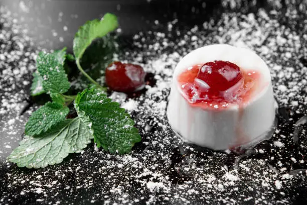 Photo of italian panna cotta dessert with strawberry sirup and mint leaf on the black wooden background