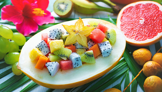 Exotic tropical fruits salad served in half a melon on leaves of palm trees