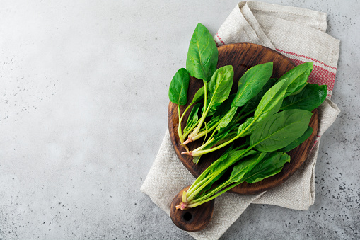 Fresh raw spinach leaves on a wooden rustic stand on a gray old concrete background. Ingredients for salad. Selective focus. Top view. Copy space.