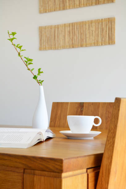 istock White ceramic cup, open book and vase on oak wood dining table 995534526
