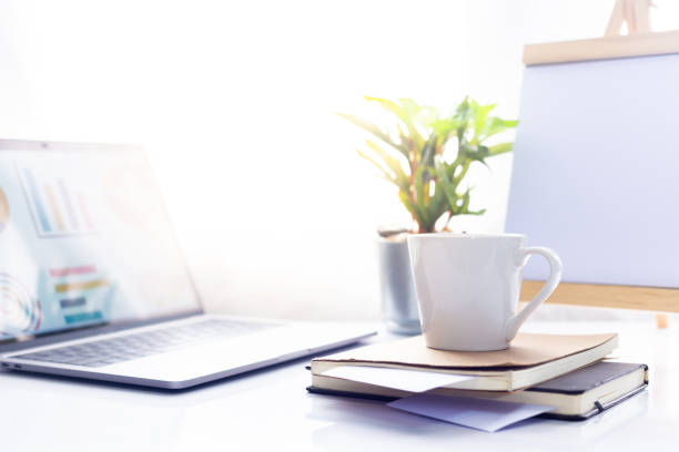istock Coffee cup on notebook with laptop on white table in the morning sun light ,Working space 995535940