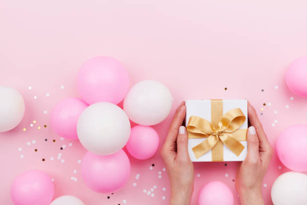 kobiety ręce gospodarstwa prezent lub obecne pudełko na różowym pastelowym stole urządzone balony i konfetti. płaski lay. - gift mothers day birthday giving zdjęcia i obrazy z banku zdjęć