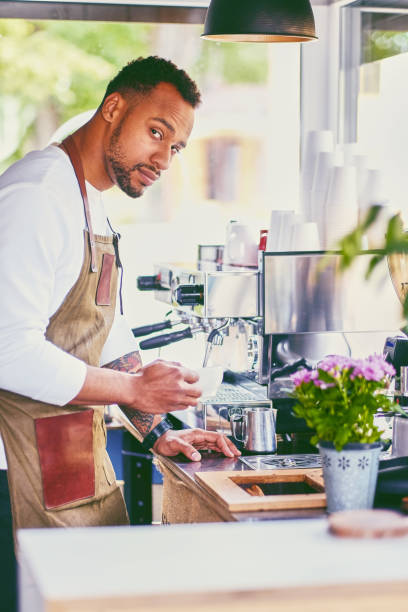 istock Black bearded coffee seller pouring coffee. 995625016