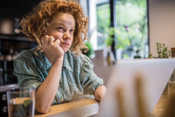 istock Pensive red-haired woman thinking while working on laptop at home. 995632690