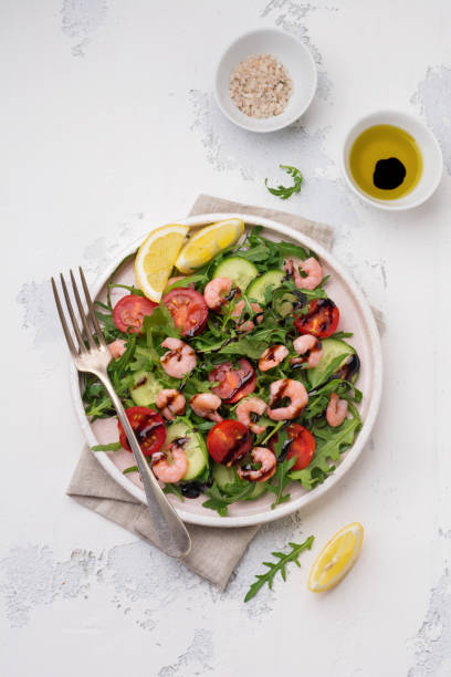 istock Arugula, cucumber, tomato and shrimp salad with soy sauce on a ceramic plate. Selective focus. Top view. 995651266