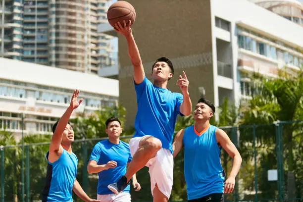 young asian adult male player playing basketball on a urban outdoor court.