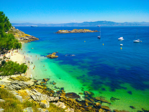 Photo of Beach with transparent green water in Cies Islands, in Galicia, Spain, with boats docked in front of