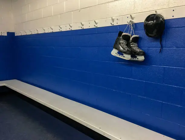 Photo of Hockey skates and helmet hanging in locker room with blue background and copy space