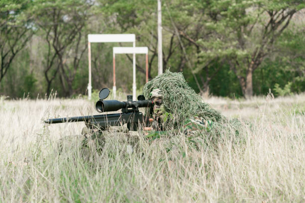 snajper żołnierz leżący na ziemi i kamuflaż w trawie. żołnierz trzymający broń i waring armor uniform. wojsko jest odpowiedzialne za utrzymanie terytorium. - cloaking zdjęcia i obrazy z banku zdjęć