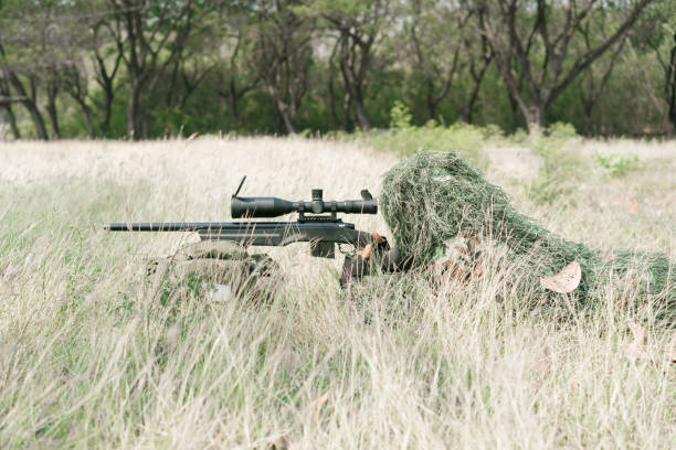 snajper żołnierz leżący na ziemi i kamuflaż w trawie. żołnierz trzymający broń i waring armor uniform. wojsko jest odpowiedzialne za utrzymanie terytorium. - cloaking zdjęcia i obrazy z banku zdjęć