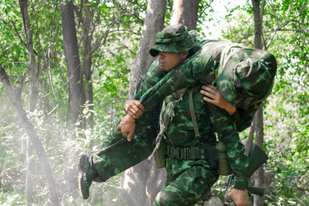 żołnierz niosący rannego człowieka z bitwy. wojsko jest odpowiedzialne za utrzymanie terytorium. żołnierz trzymający broń i waring armor uniform. - cloaking zdjęcia i obrazy z banku zdjęć