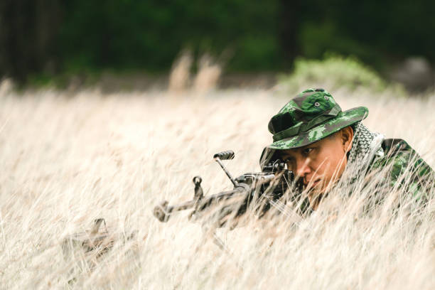 żołnierz leżący na ziemi i kamuflaż w trawie. żołnierz trzymający broń i waring armor uniform. wojsko jest odpowiedzialne za utrzymanie terytorium. - cloaking zdjęcia i obrazy z banku zdjęć